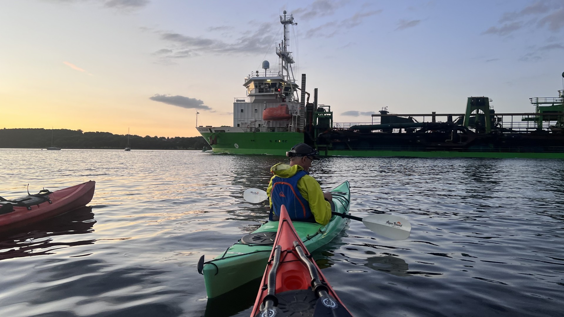 A dredger passing sea kayakers with NOMAD Sea Kayaking.