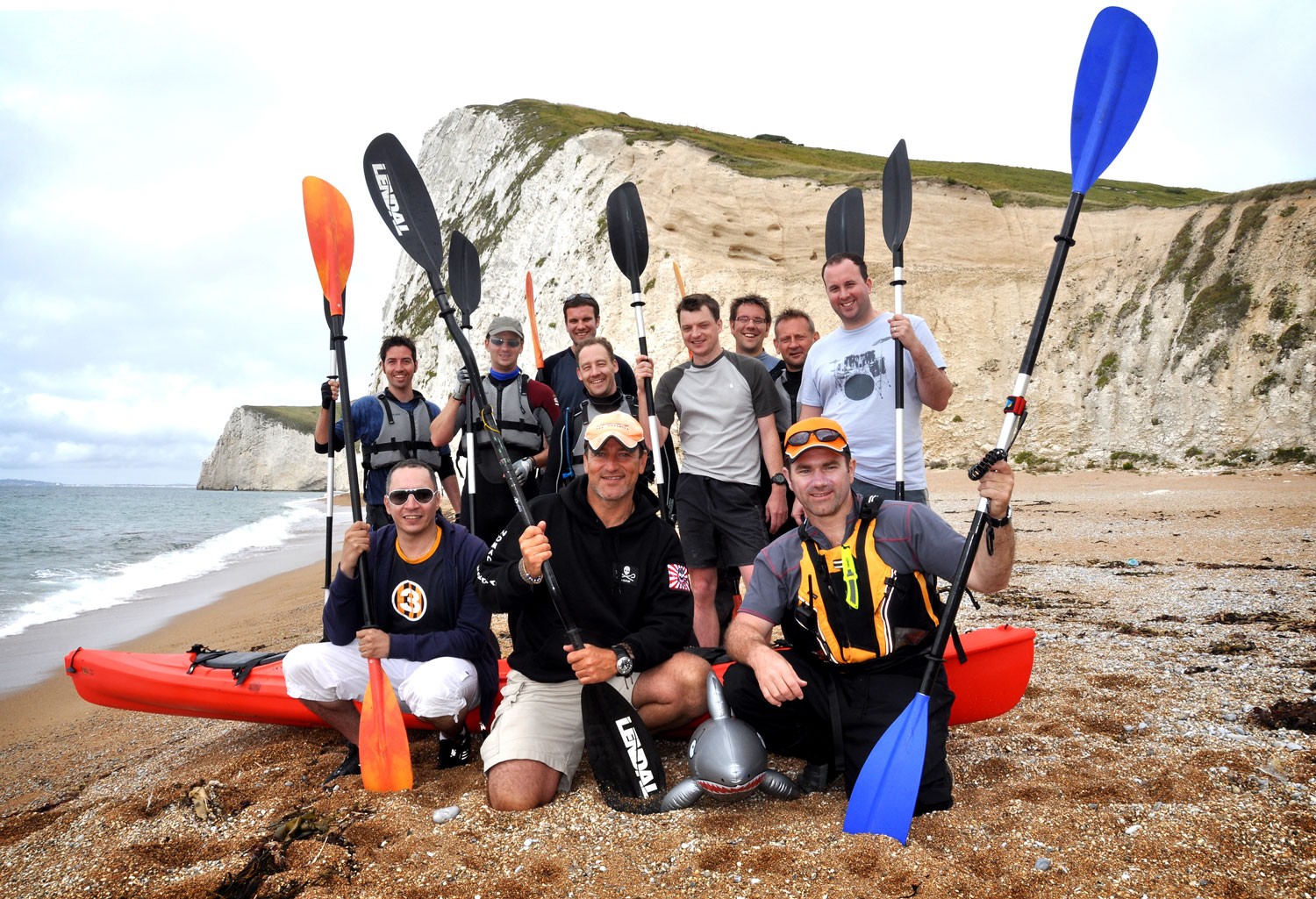 A happy group posing on a beach with kayaks and paddles private tailored events