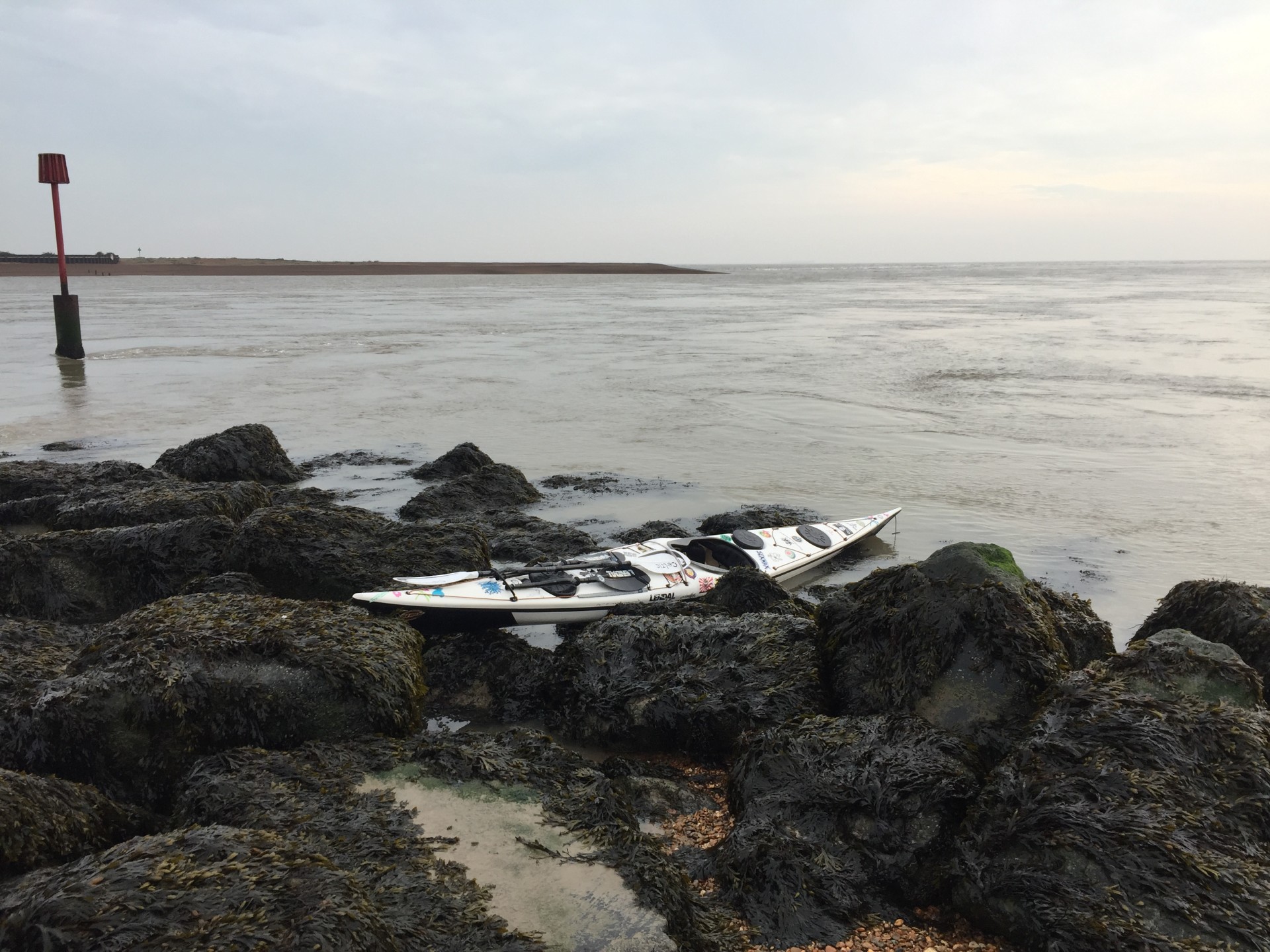 Sea kayak pulled up onto rocks on an estuary in Suffolk.