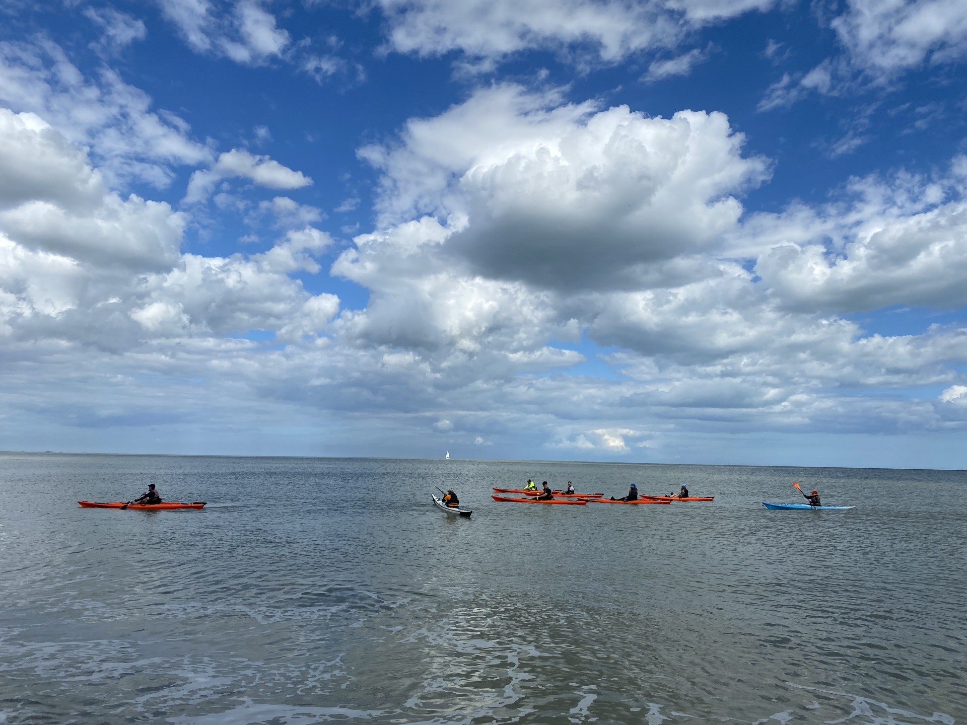 Group of kayakers on flat calm seas with blue skies.