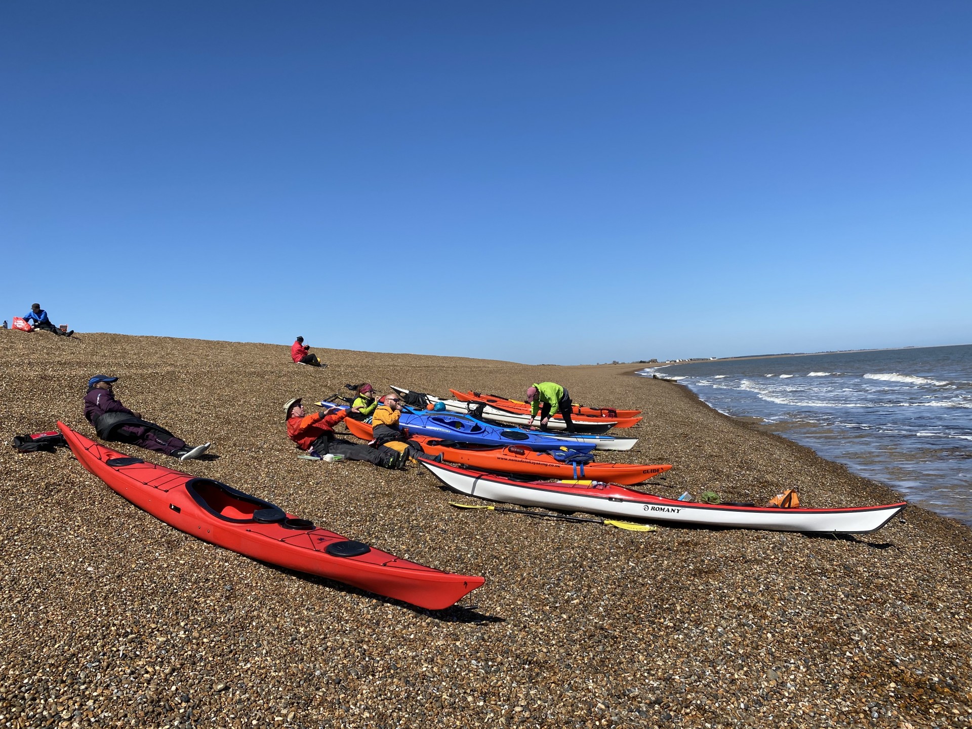 Sea kayakers enjoying the sunshine on a shingle beach in Suffolk.